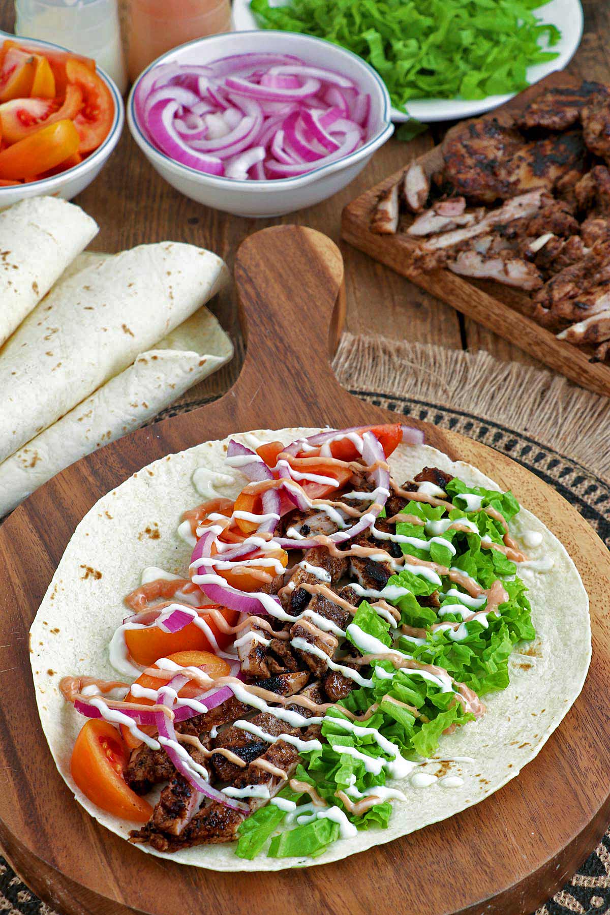 Unwrapped Chicken Shawarma with tomatoes, onions, and lettuce on top of tortilla wrap.